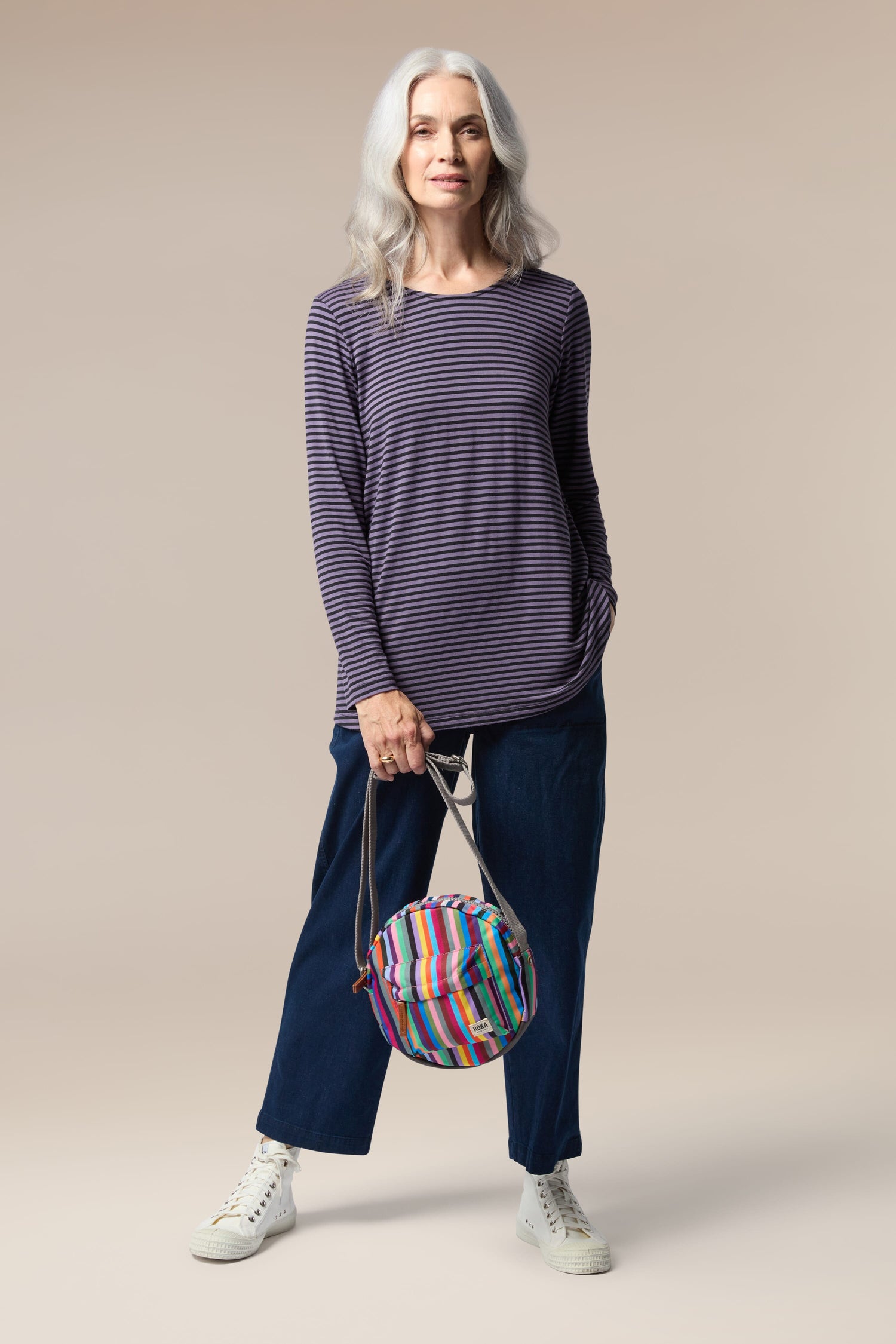 A woman in a purple top and blue pants holding a lightweight handbag, perfect for the weather-resistant Recycled Canvas Paddington Bag.