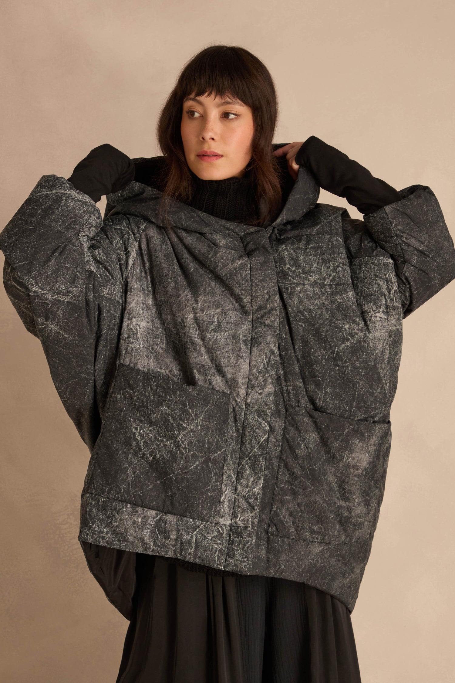 A model wearing an Asymmetric Hooded Puffer Jacket featuring a dark grey, textured marble-like pattern.