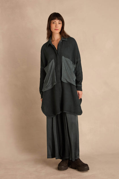 A person wearing an oversized, crinkled Petrol Pocket Satin shirt with large front pockets and a matching long skirt, paired with dark platform boots.
