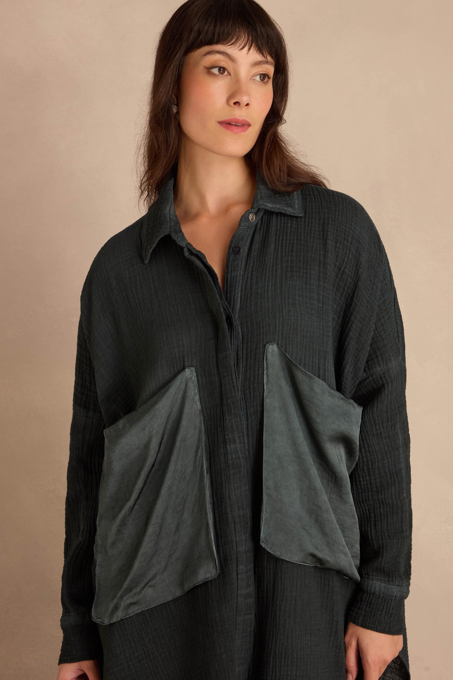 A person wearing a Petrol Pocket Satin Shirt in an oversized fit, dark grey, button-down crinkled cotton with two large, contrasting pockets.