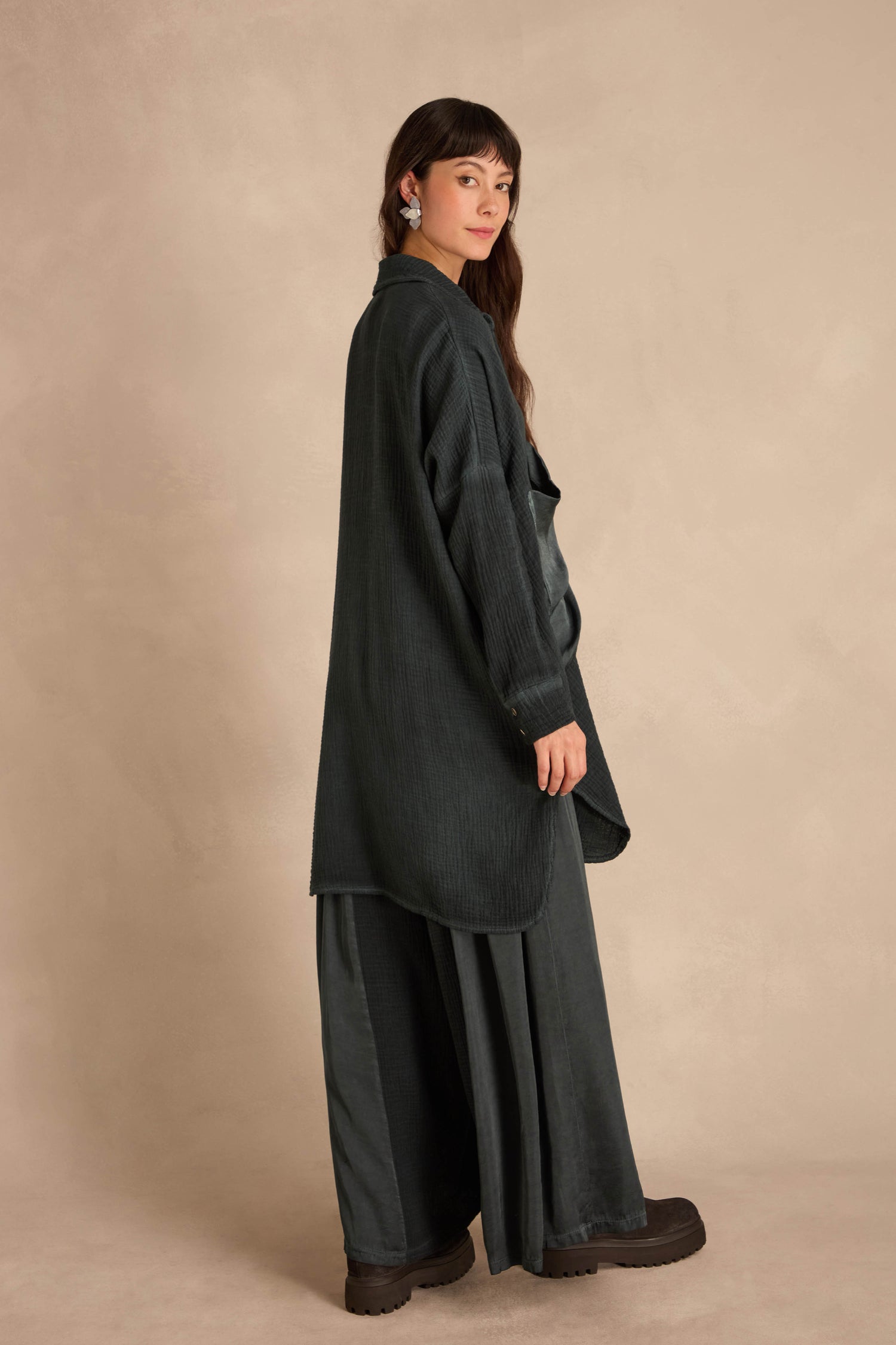 A person wearing an oversized Petrol Pocket Satin Shirt over a matching skirt and dark platform shoes.