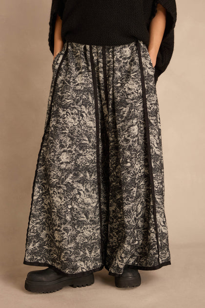 Frayed Hem Wide Leg Trousers in a cotton-rich woven fabric with a black and white floral pattern, black side panels, and frayed hems, worn with chunky black shoes.