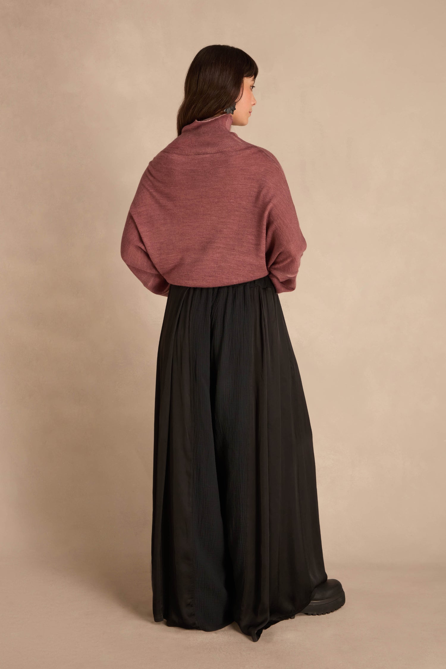 A person seen from behind, wearing a dusty rose cowl-neck sweater and Black Wide Leg Panel Trousers.