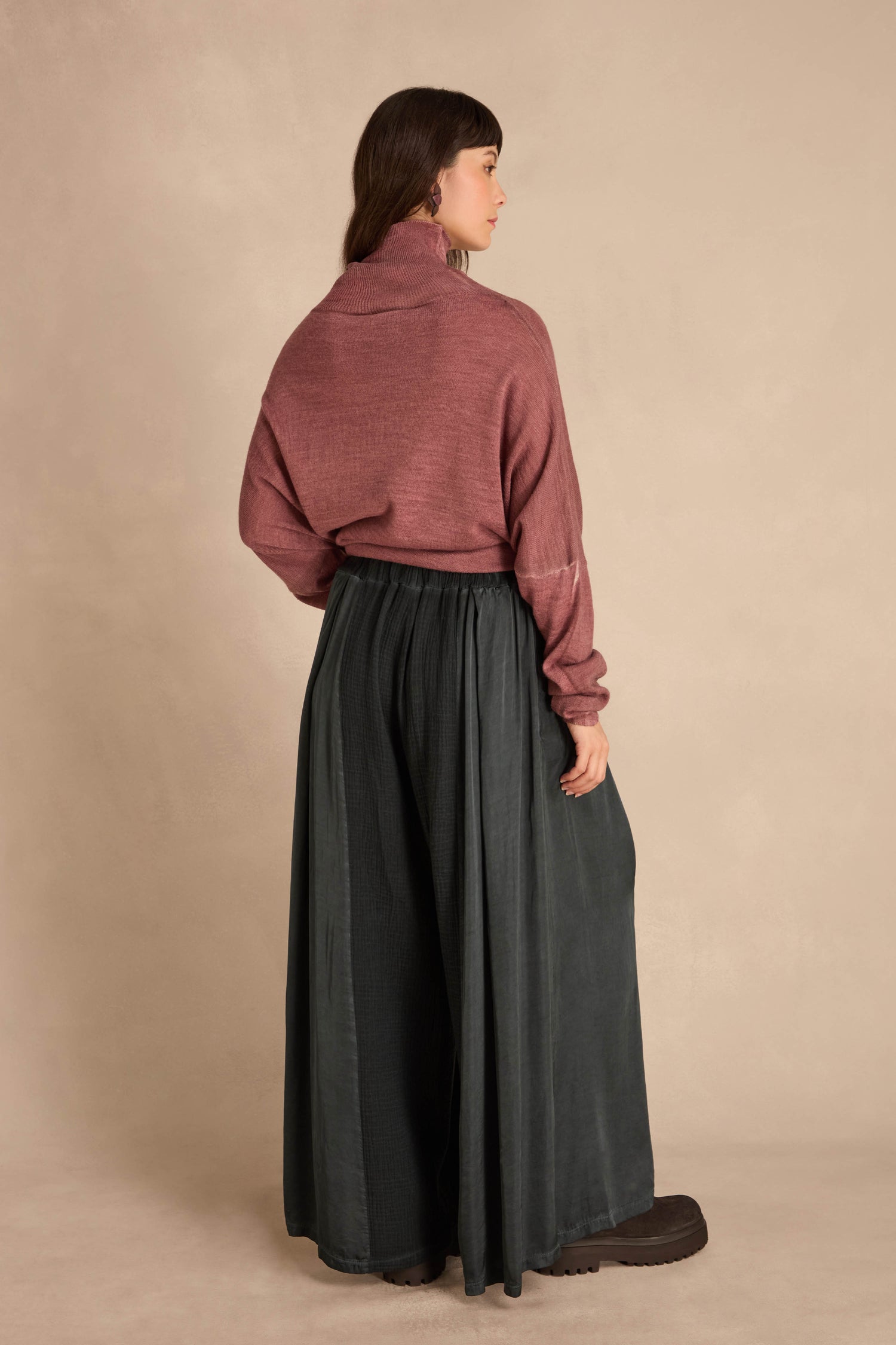 A person wearing a dusty rose cowl-neck sweater and Petrol Wide Leg Panel Trousers in washed blue-green.