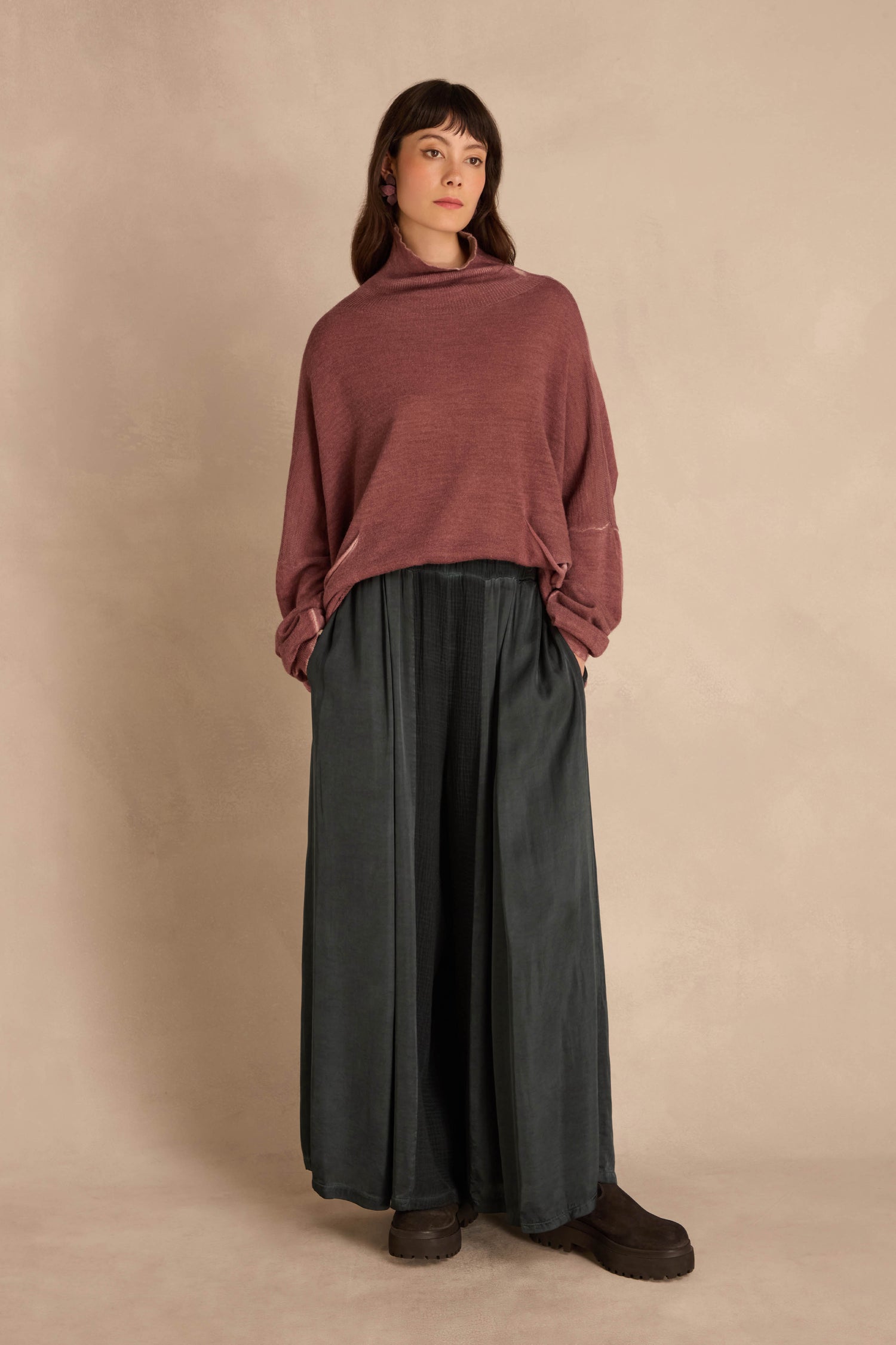 A person wearing a dusty rose long-sleeved sweater and Petrol Wide Leg Panel Trousers in dark green, featuring a gathered waist and vertical panel detailing.