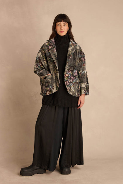 A person wearing a Tapestry Jacket over a black turtleneck sweater and wide-leg black trousers.