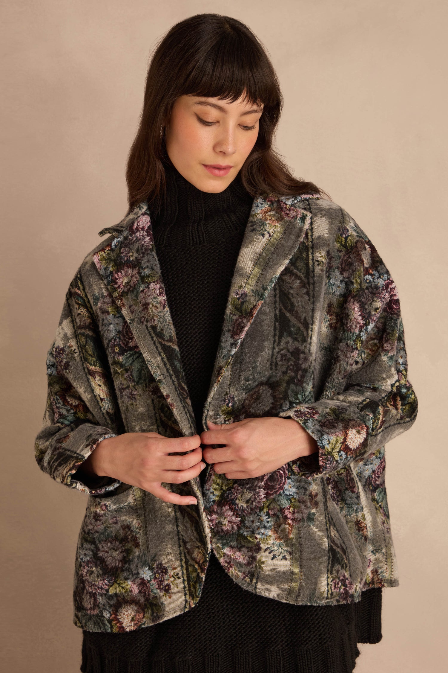 A person wears a grey floral Tapestry Jacket over a black turtleneck sweater.