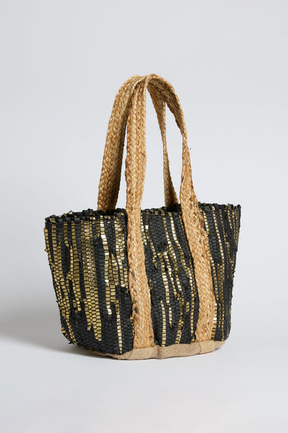 The Black and Gold Upcycled Leather Tote Bag features wide, braided handles and a striking black and gold sequin striped pattern, showcasing sustainable craftsmanship with a handwoven design.
