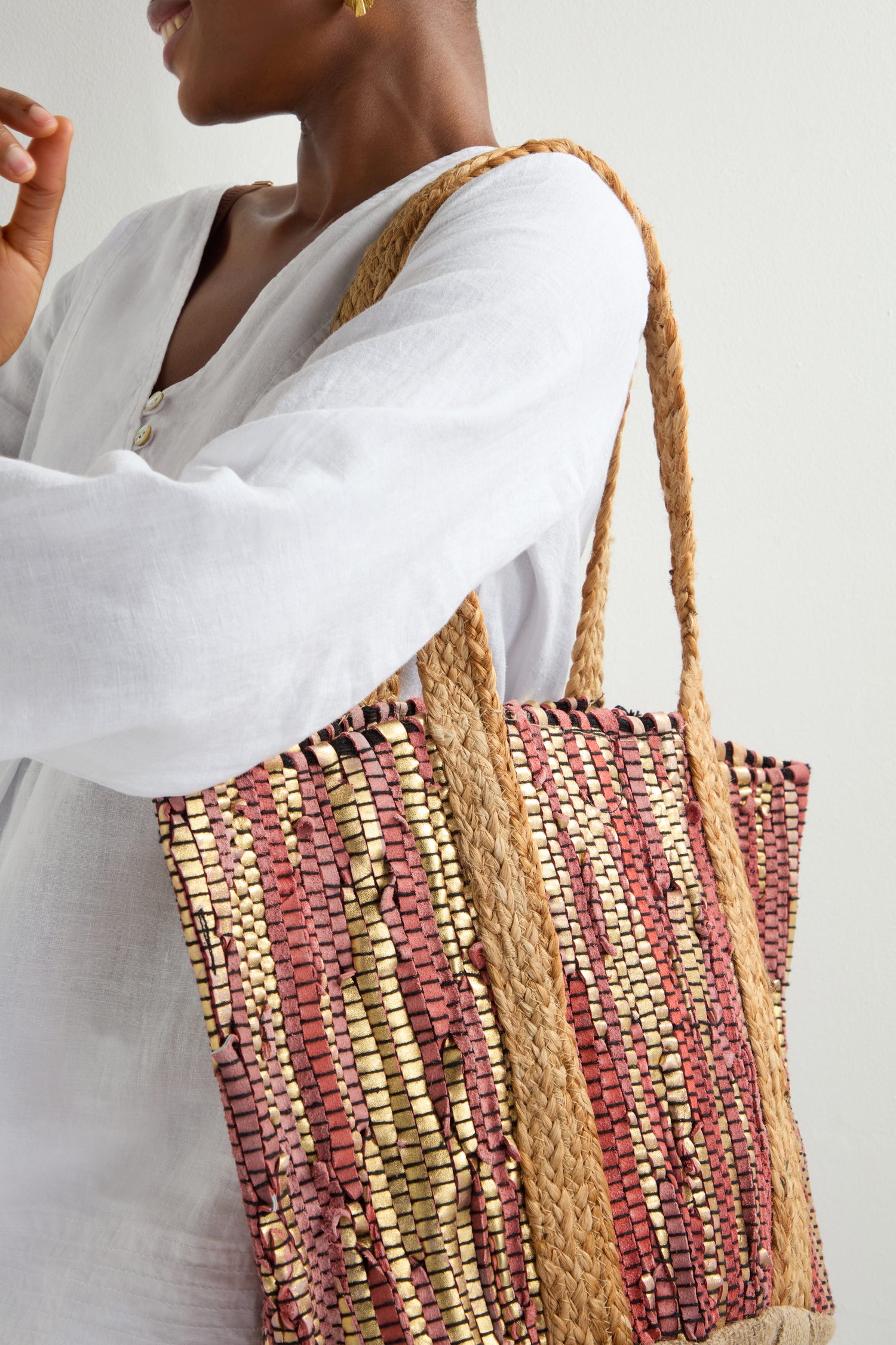 A person in a white long-sleeve shirt holds the Rose Upcycled Leather Tote Bag with earth-toned patterns and large rope handles. Handmade in India, its intricate design showcases sustainable craftsmanship as they face away from the camera.