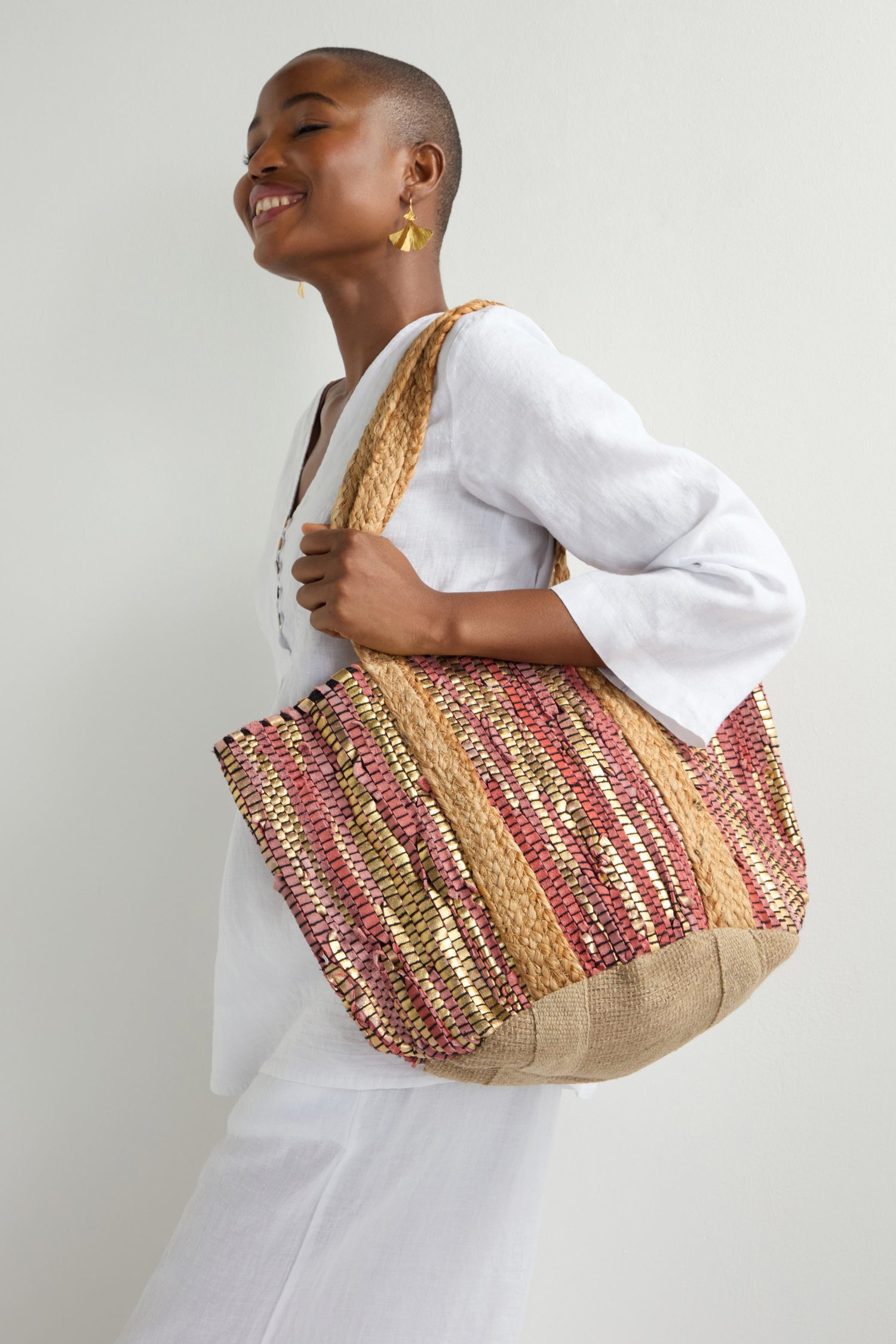 A person in white smiles, carrying the Rose Upcycled Leather Tote Bag, featuring a large design with multicolored patterns and thick handles that embody sustainable craftsmanship.