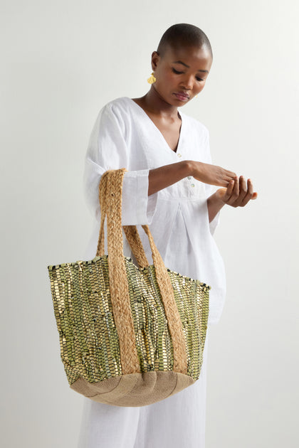 A person in a white dress holds the Sage Upcycled Leather Tote Bag, featuring green and beige patterns crafted with sustainable techniques, against a plain background.