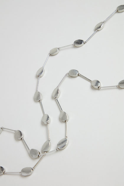 The Long Oval Disc Necklace showcases textured oval discs and slim connecting bars, elegantly displayed on a white background.