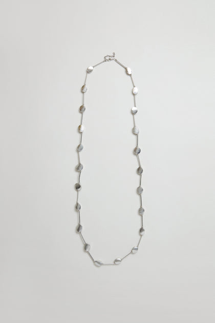 The Long Oval Disc Necklace features textured silver oval discs evenly spaced along a thin chain, shown against a plain light background.