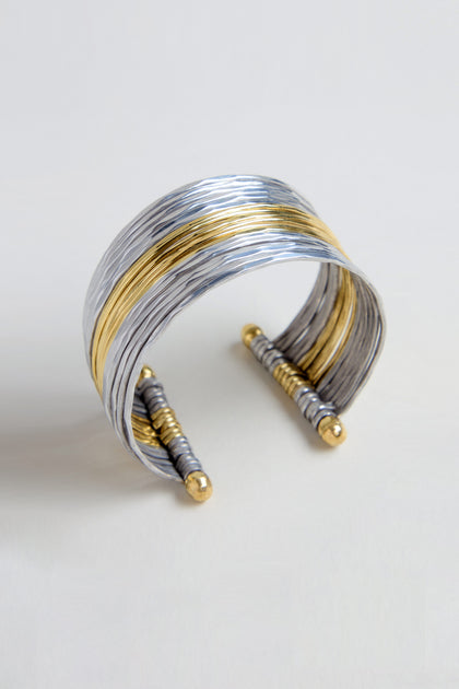 The Mixed Metal Cuff is a wide, open bracelet with layered silver and gold bands and gold-accented ends, shown against a light background.