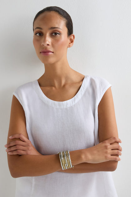 A woman with dark hair pulled back, wearing a white sleeveless top and the Mixed Metal Spiral Cuff, stands against a white wall with her arms crossed.
