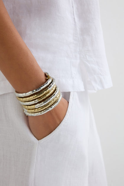 A person in a white outfit slips a hand into their pocket, highlighting the Mixed Metal Spiral Cuff on their wrist. The bracelet’s gold and silver tones add an artistic flair to the sculptural silhouette.