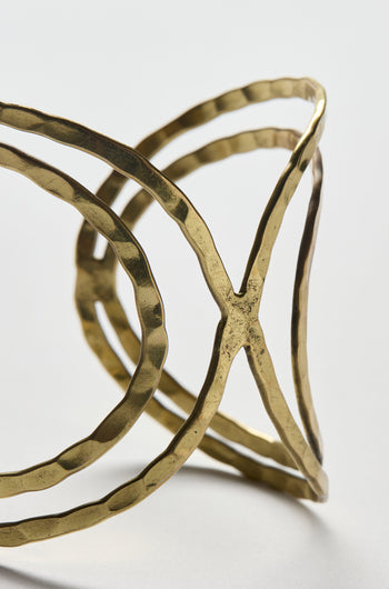 Close-up of the Butterfly Bangle, a gold-toned cuff bracelet featuring a hammered finish and open geometric design, displayed on a plain light background.