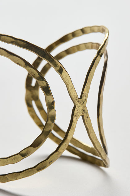 Close-up of the Butterfly Bangle, a gold-toned cuff bracelet featuring a hammered finish and open geometric design, displayed on a plain light background.