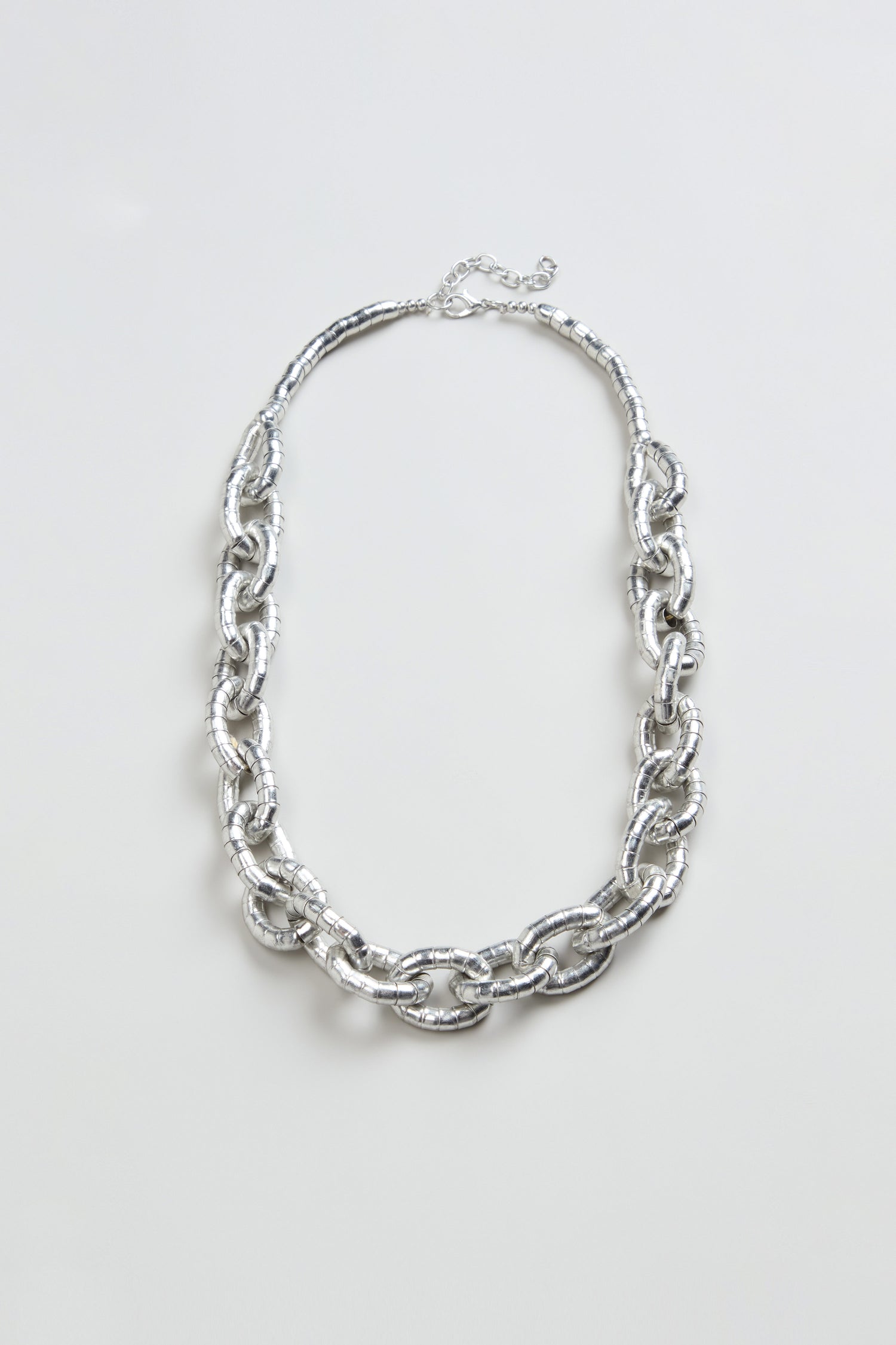 The Soft Loops Necklace, featuring large textured silver-toned oval links, is showcased on a plain light background.