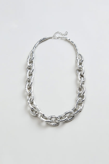 The Soft Loops Necklace, featuring large textured silver-toned oval links, is showcased on a plain light background.