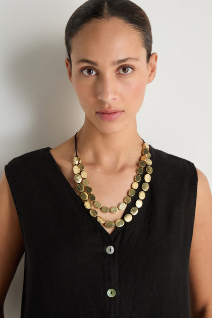 A woman wearing a sleeveless black top and the Double Strand Oval Disc Necklace stands against a plain white background.