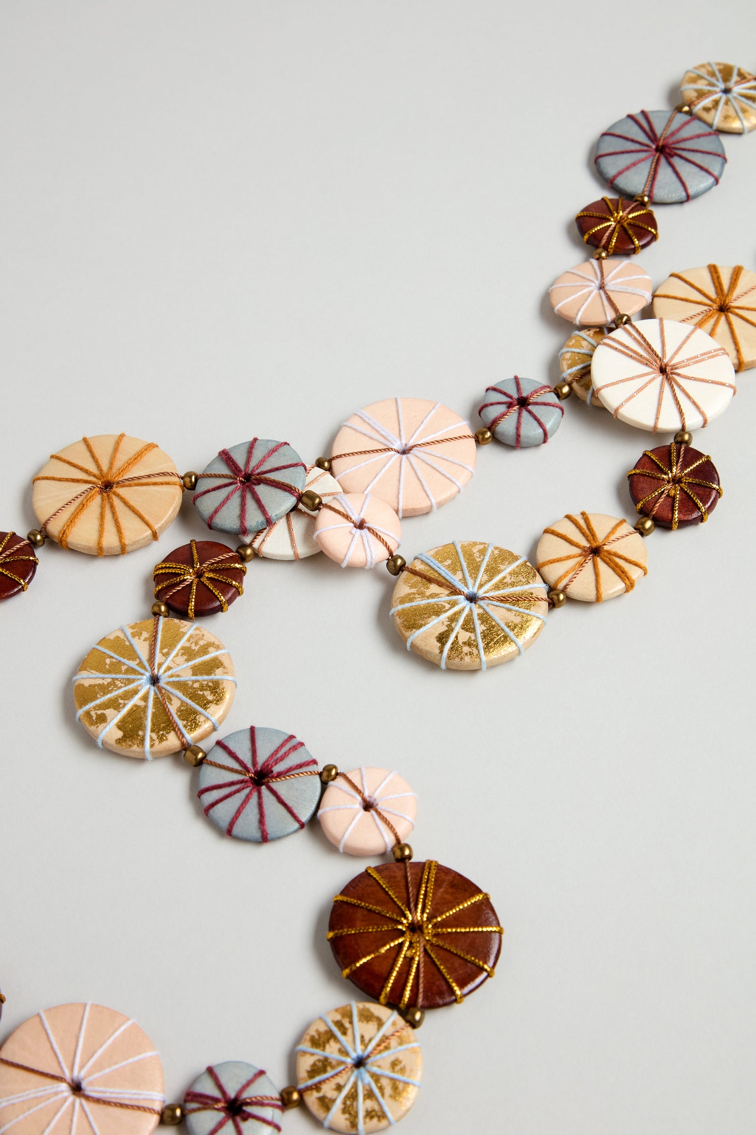 The Long Wooden Metallic Parasols Necklace features round, fabric-covered beads in gold, brown, pink, and gray cotton detail, displayed on a neutral background.