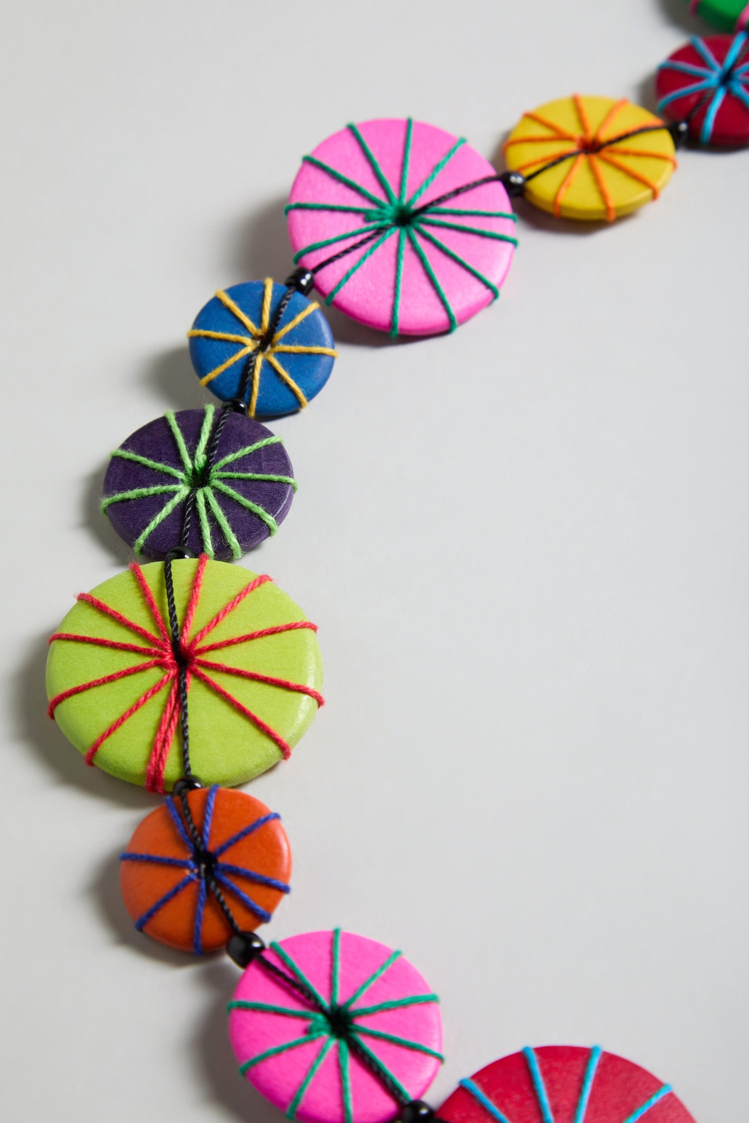 A close-up of the Long Wooden Disc Necklace showcases colorful, handmade round flat wooden beads with intricate thread wrap detail, displayed against a plain light background.