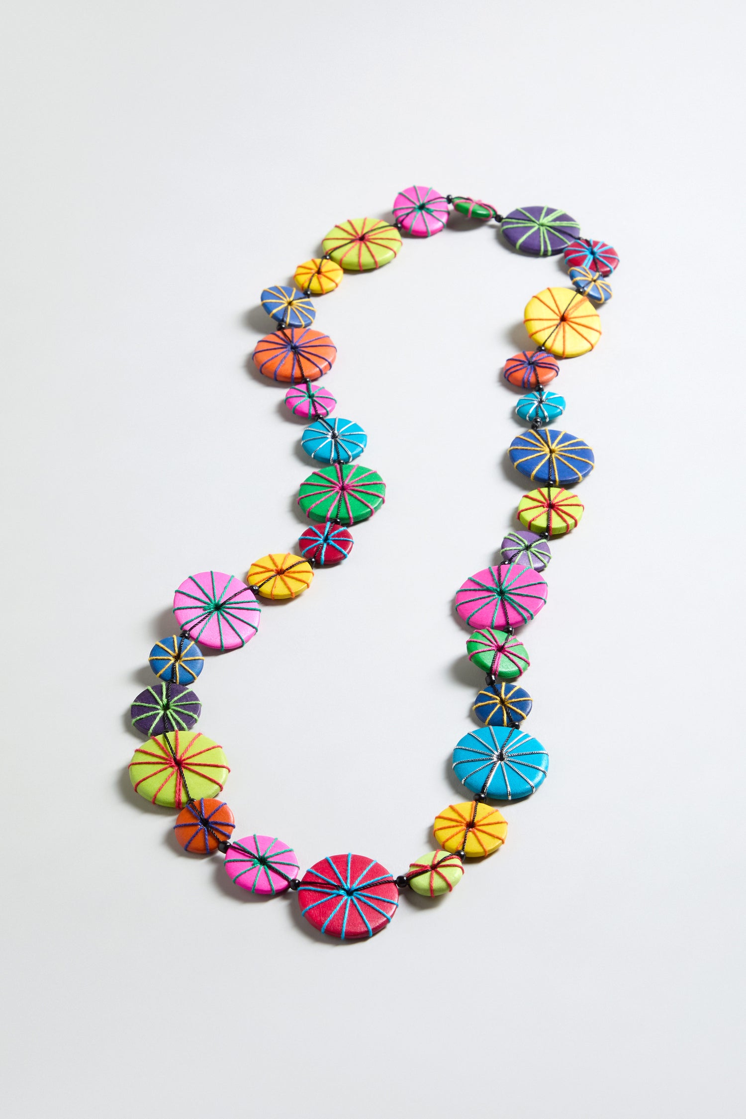 The Long Wooden Disc Necklace showcases circular, multicolored wooden beads with stitched radial patterns and thread wrap accents, arranged in a single strand on a plain light background.