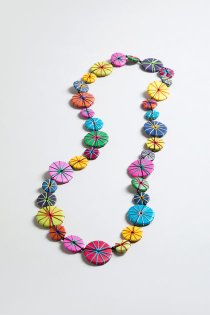 The Long Wooden Disc Necklace showcases circular, multicolored wooden beads with stitched radial patterns and thread wrap accents, arranged in a single strand on a plain light background.