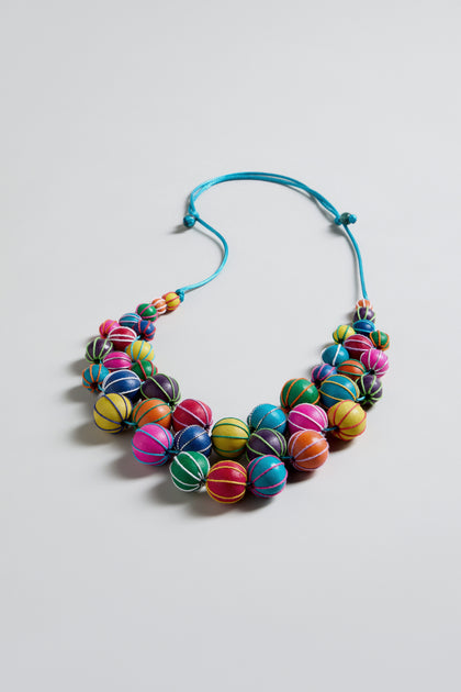 The Rainbow Wooden Spheres Necklace features rainbow-hued wooden beads, each wrapped with thread and strung on a light blue adjustable cord, shown against a plain white background.