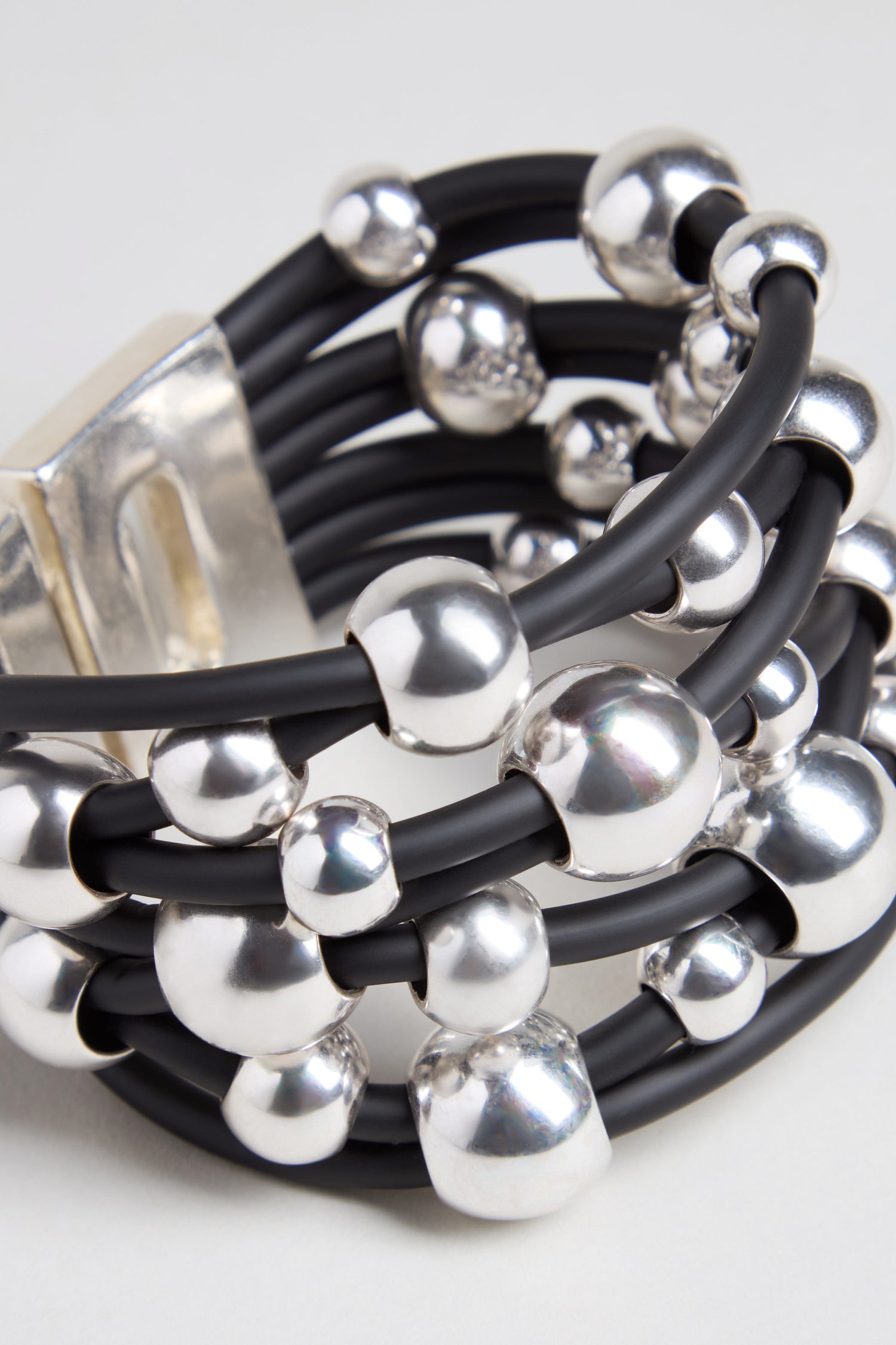 Introducing the Metal Spheres Bracelet: a sculptural, contemporary piece handmade in France. This refined bracelet features multiple black bands interwoven with shiny silver spheres and finished with a bold metallic clasp, highlighting exquisite craftsmanship throughout.