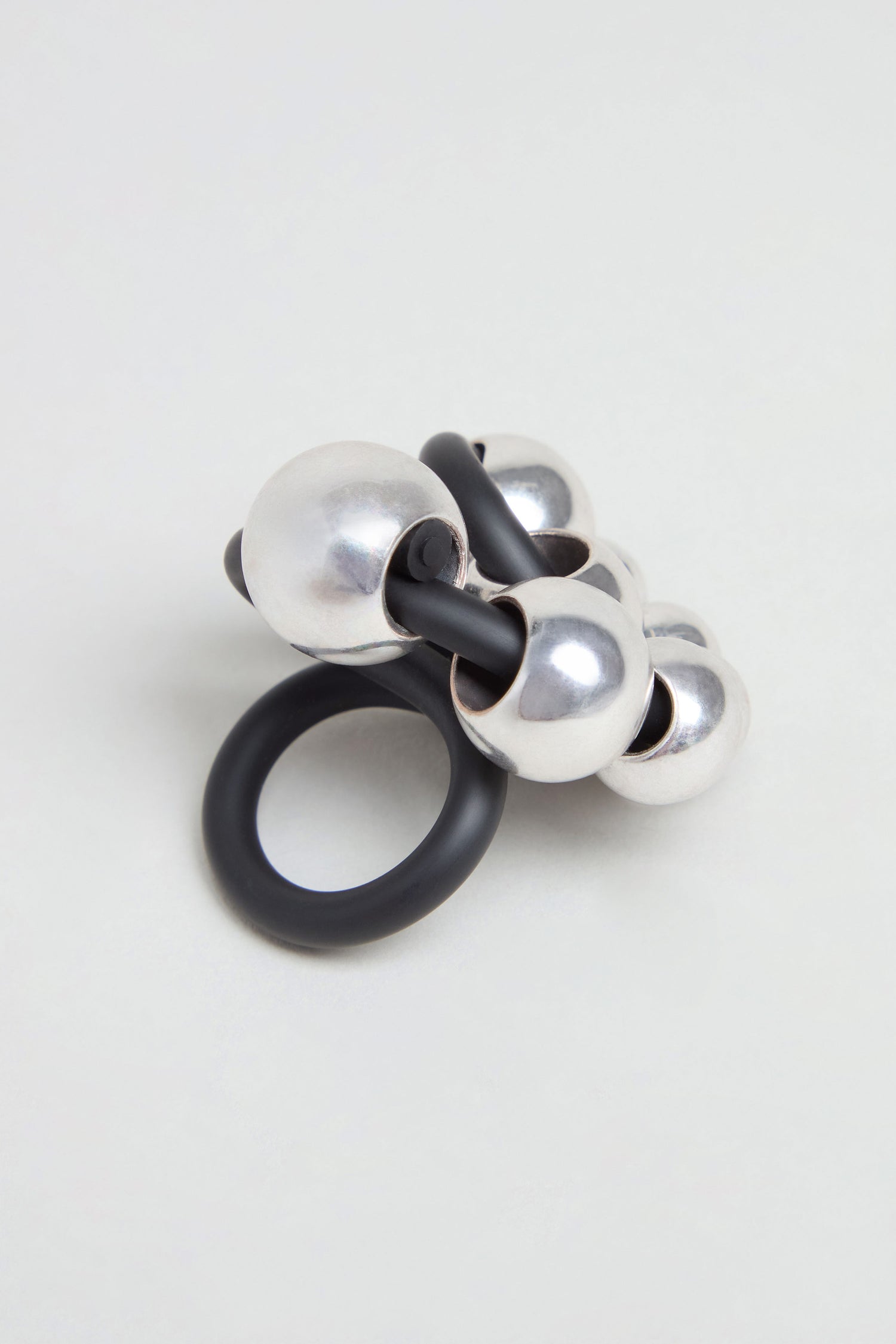 The Metal Spheres Adjustable Ring showcases a sculptural design with interconnected black and silver metallic spheres, elegantly displayed on a plain light background.