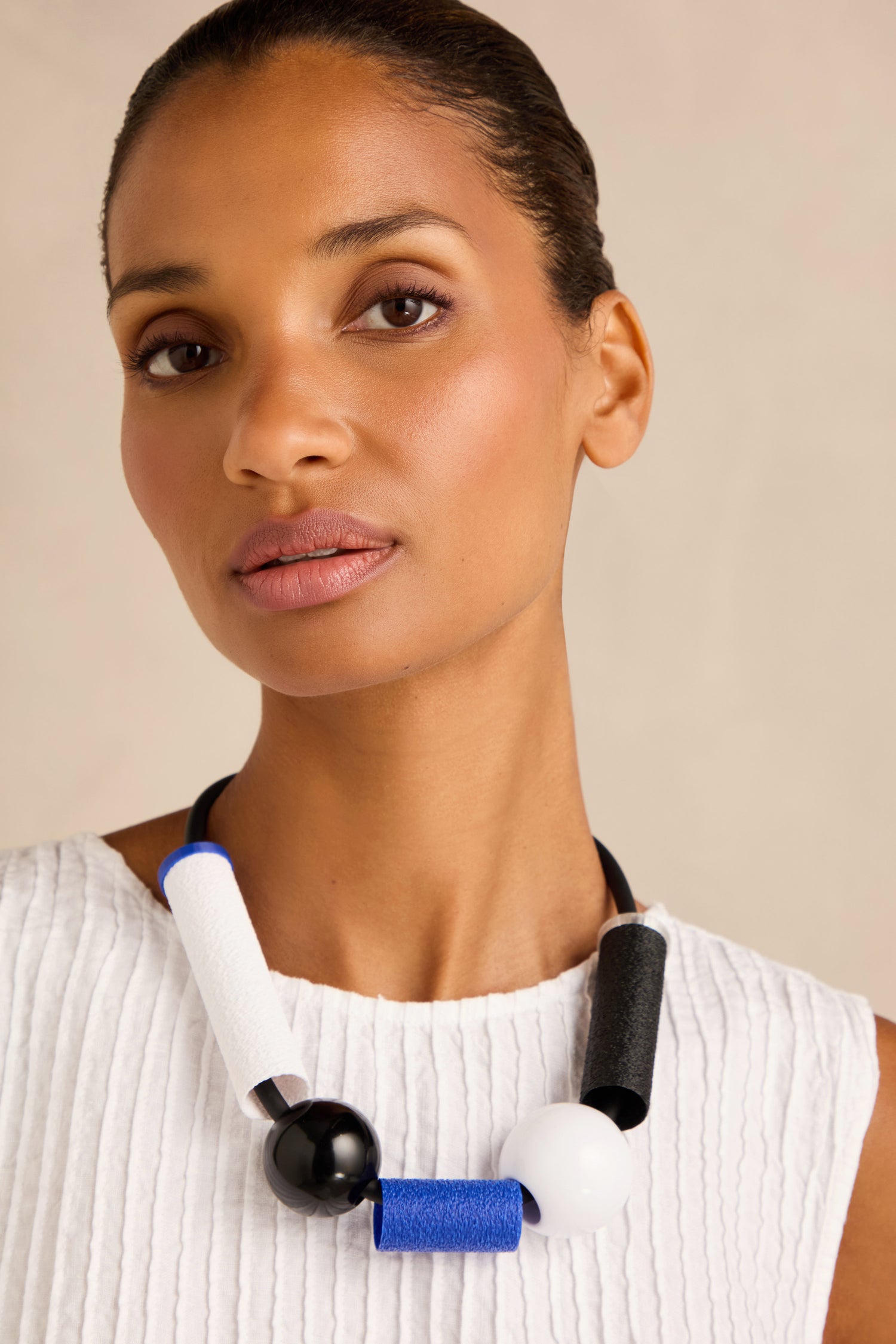 A woman wearing a white textured top and the Colour Block Necklace, a handmade contemporary piece from France featuring large black, white, and blue geometric beads.