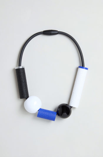 Introducing the Colour Block Necklace: a chunky, contemporary piece handmade in France. This modern geometric design features a black cord, two large statement beads (one white and one black), and three textured cylindrical segments in black, blue, and white—creating striking colour contrasts for wearable art.