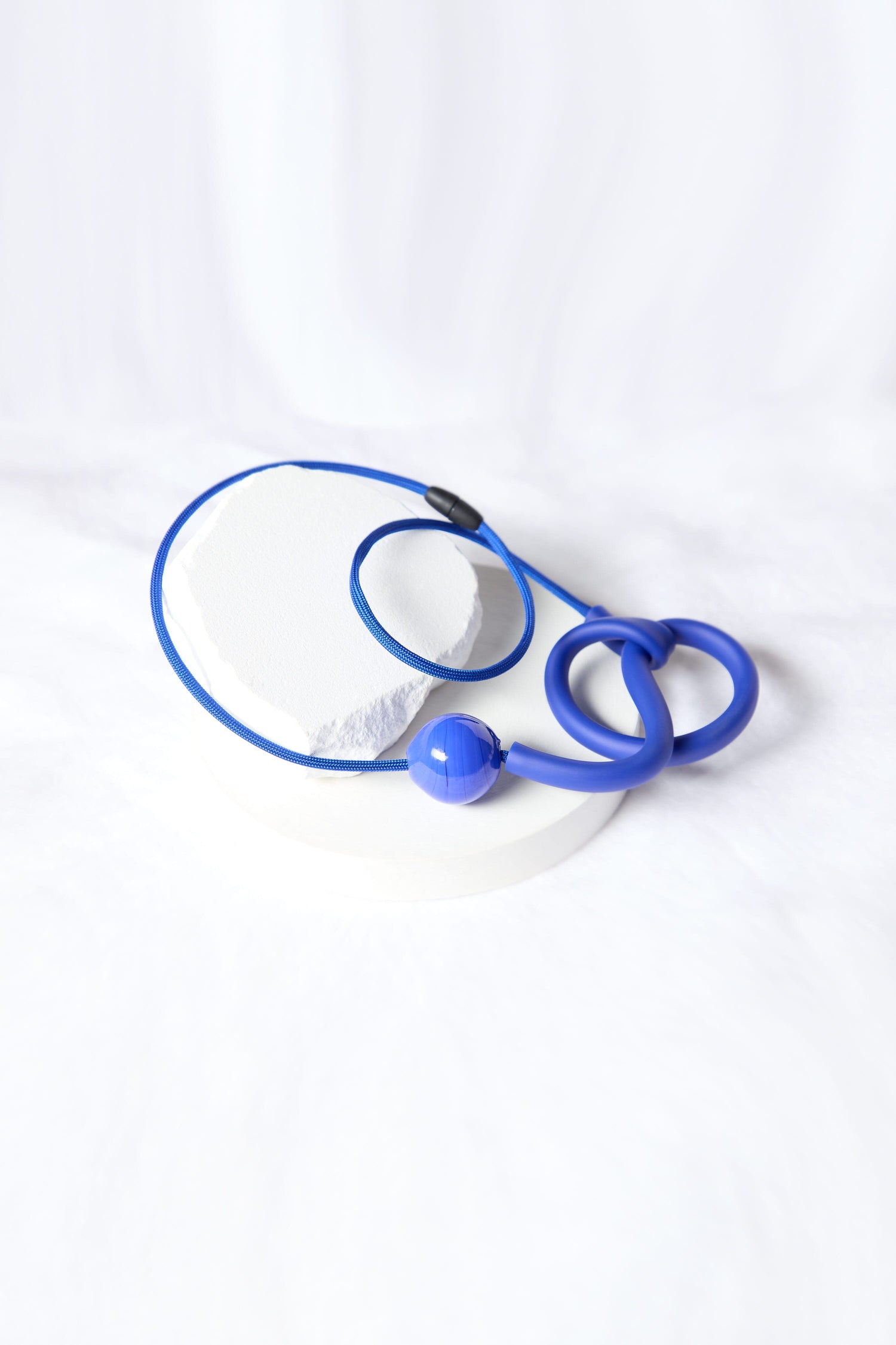 A blue stethoscope lies coiled on a white surface with a soft, blurred background, resembling the elegance of a Murano Glass Knot Necklace.