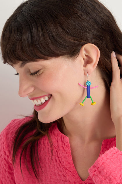 A woman with brown hair smiles, wearing a bright pink textured top and the Beautiful People Earrings—colorful, abstract, handmade in Paris—for a charming, playful touch while she holds a hand near her ear.