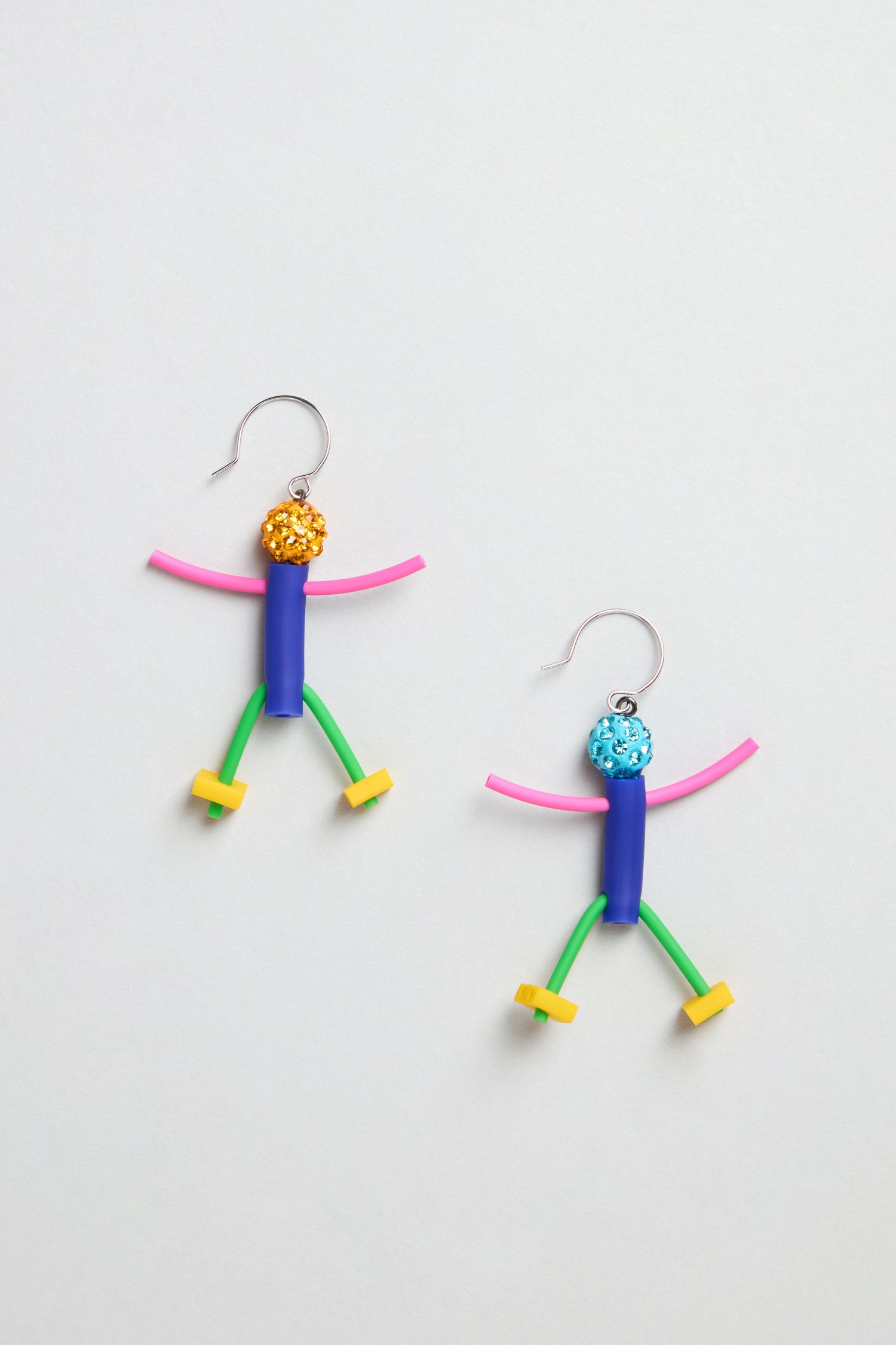 Beautiful People Earrings: Handmade in Paris, these colorful abstract stick figure earrings feature a yellow head on one and a blue head on the other, each with a curved hook—displayed on a white background.