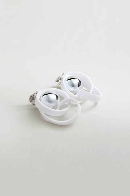 The Silver Sphere Penseur Earrings feature shiny silver spheres wrapped in overlapping white loops with a modern, lightweight design, shown against a light, neutral background.
