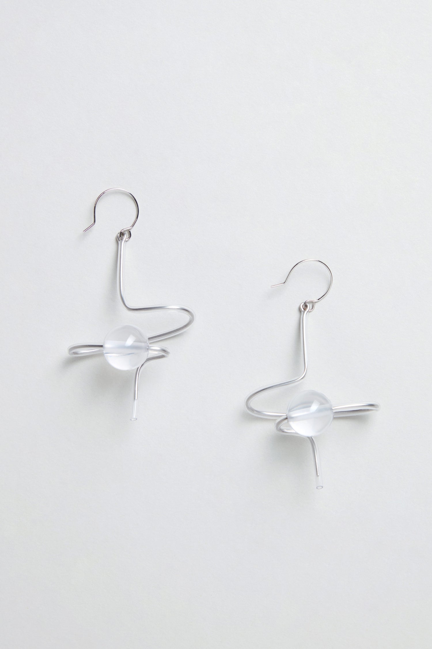 The Sketch Ball Earrings are handmade in Paris, featuring a silver sculptural form with abstract swirling shapes and a clear round bead at the center.