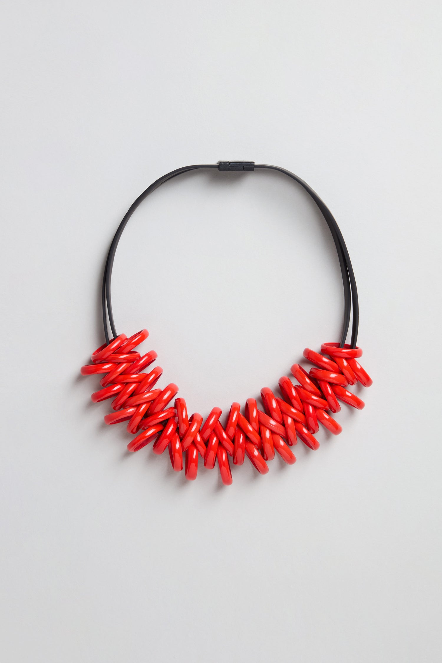The Murano Links Necklace features glossy red oval Murano glass beads clustered on a black cord, creating a bold statement piece, shown against a light gray background.