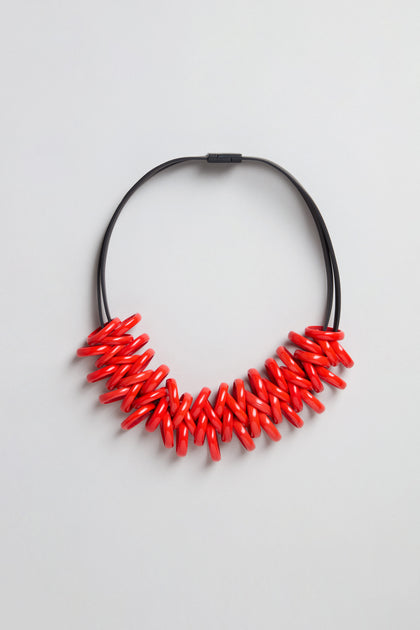 The Murano Links Necklace features glossy red oval Murano glass beads clustered on a black cord, creating a bold statement piece, shown against a light gray background.