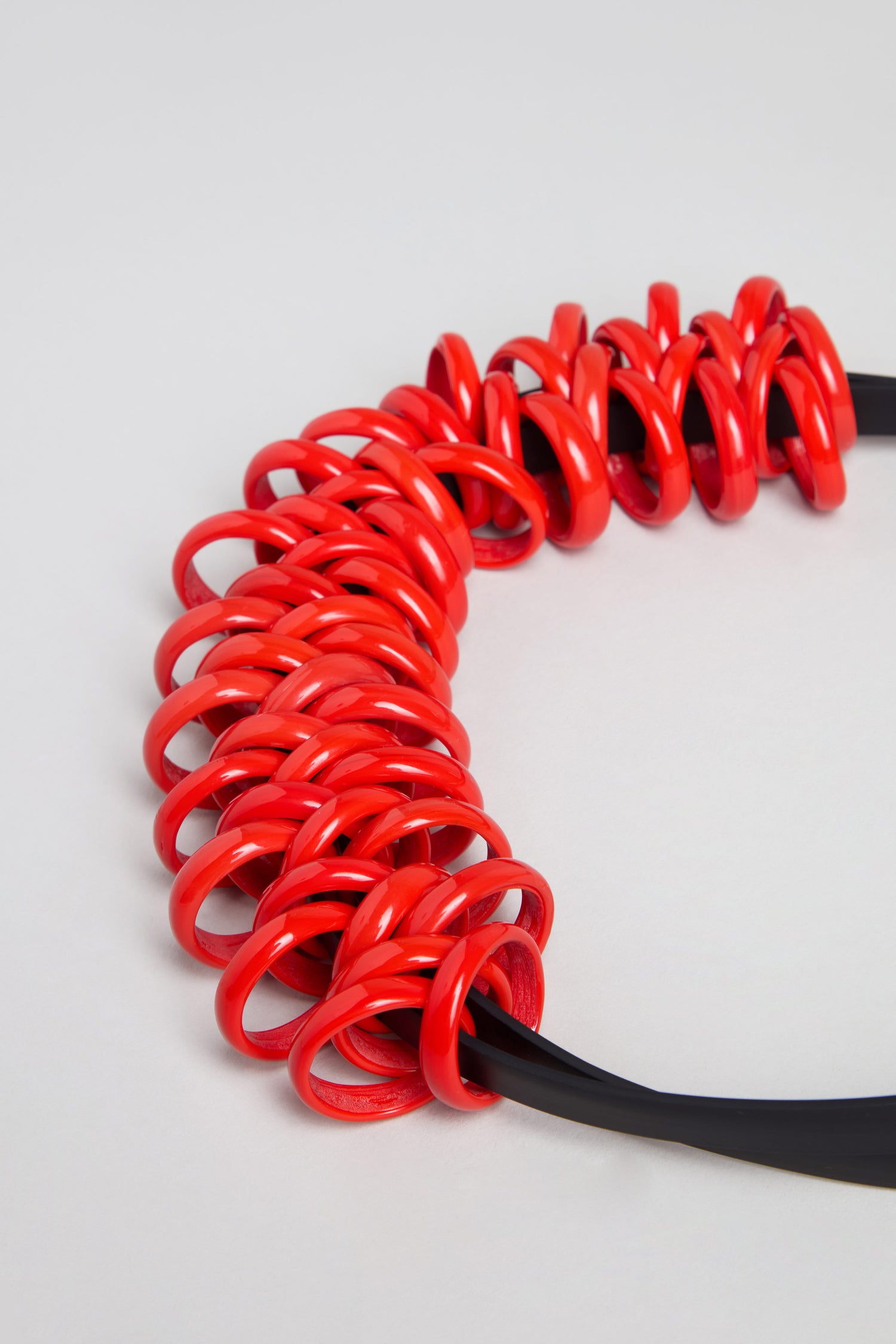 Make a bold statement with the Murano Links Necklace. Handmade in Paris, this black cord necklace showcases multiple shiny red spiral rings grouped on one side for a striking touch to any outfit. Displayed on a light background.
