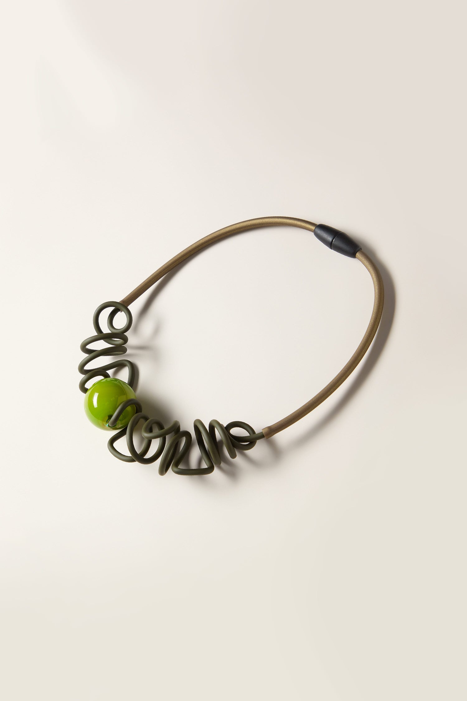 A Murano Sketch Necklace featuring a green beaded design with thick, curly green spirals reminiscent of Samuel Coraux's unique style, completed with a beige elastic band and a black connector.