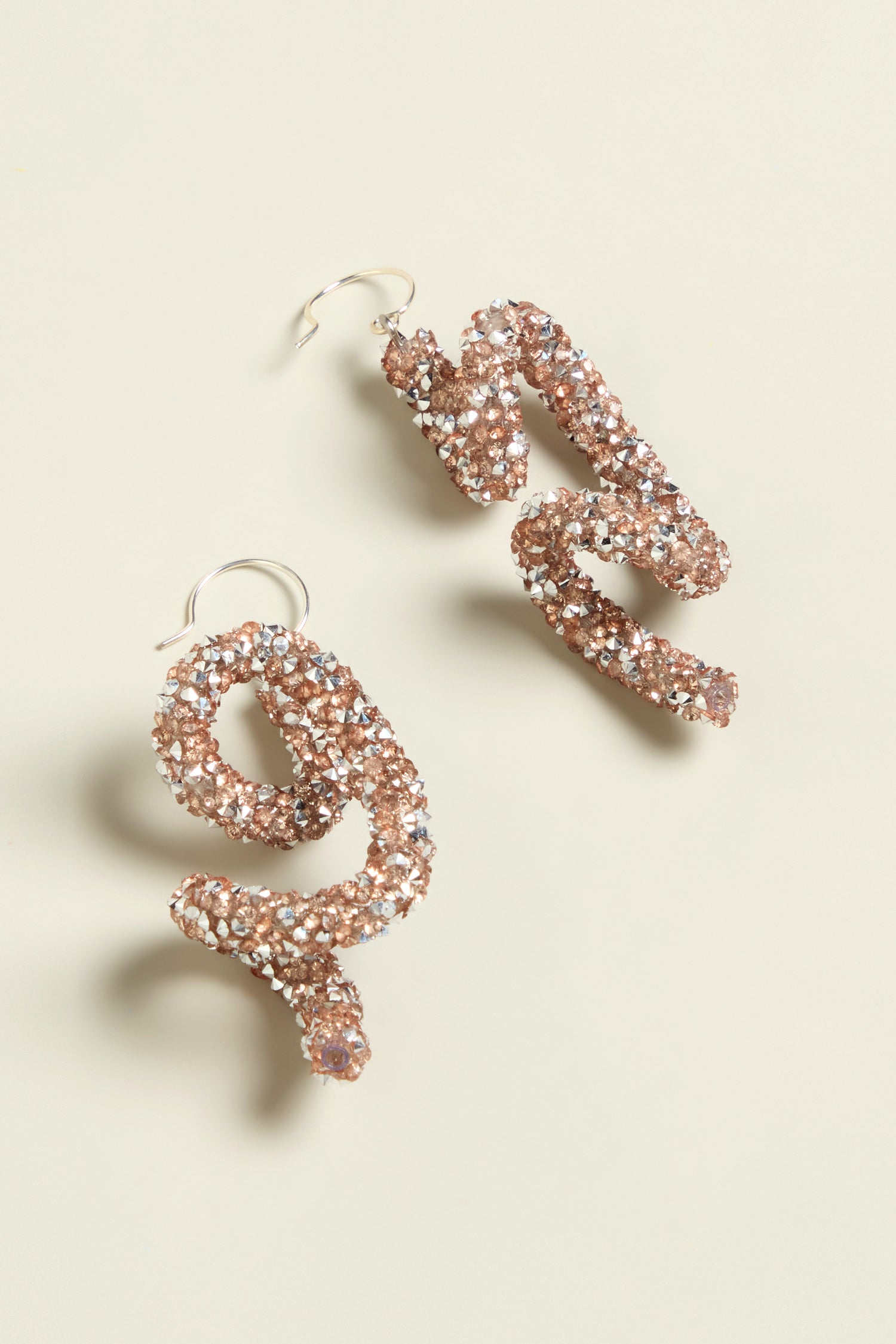 Set against a light gray background, the Disco Sketch Earrings by Samuel Coraux create an artistic impression with their gold, glittery, snake-like design.