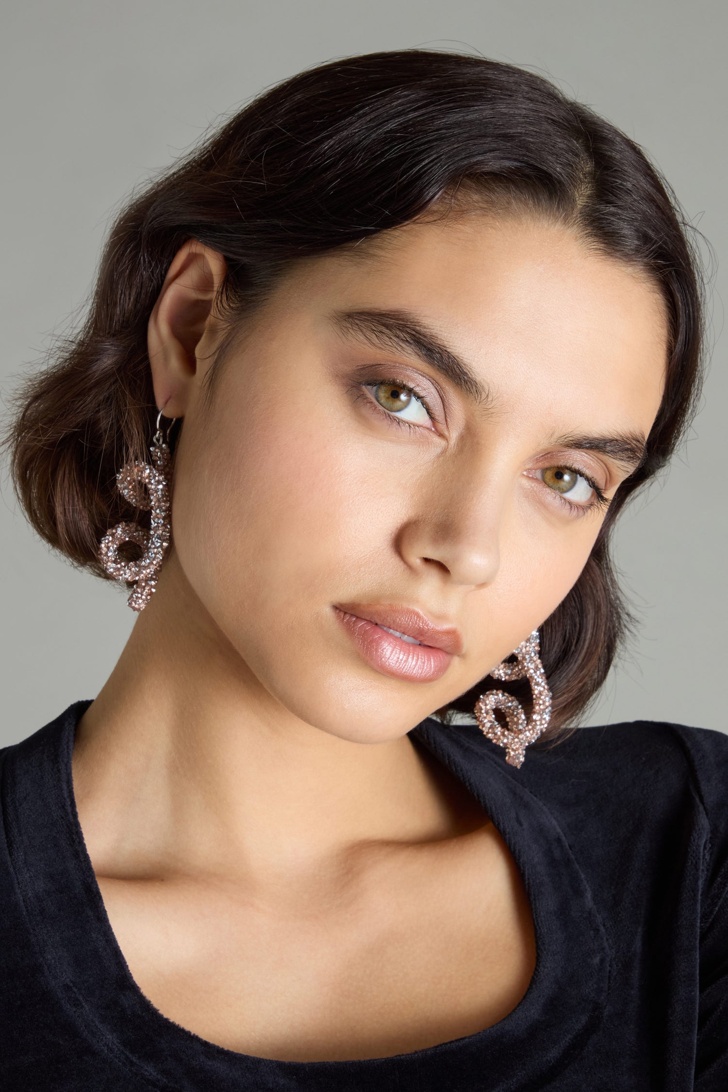 A person with short dark hair is making an artistic statement while wearing the Disco Sketch Earrings by Samuel Coraux and a black top, gazing directly at the camera against a plain background.