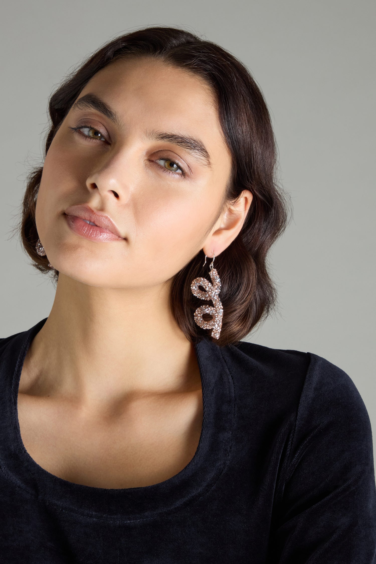 A person with short dark hair and a black top showcases the striking Disco Sketch Earrings, creating an artistic statement against a gray background.