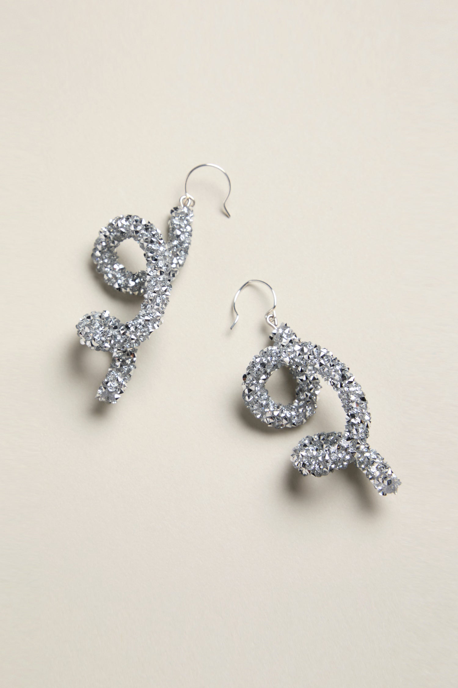 A pair of silver glitter twist earrings, artfully showcased on a light background, evoke the artistic flair of the Disco Sketch Earrings.