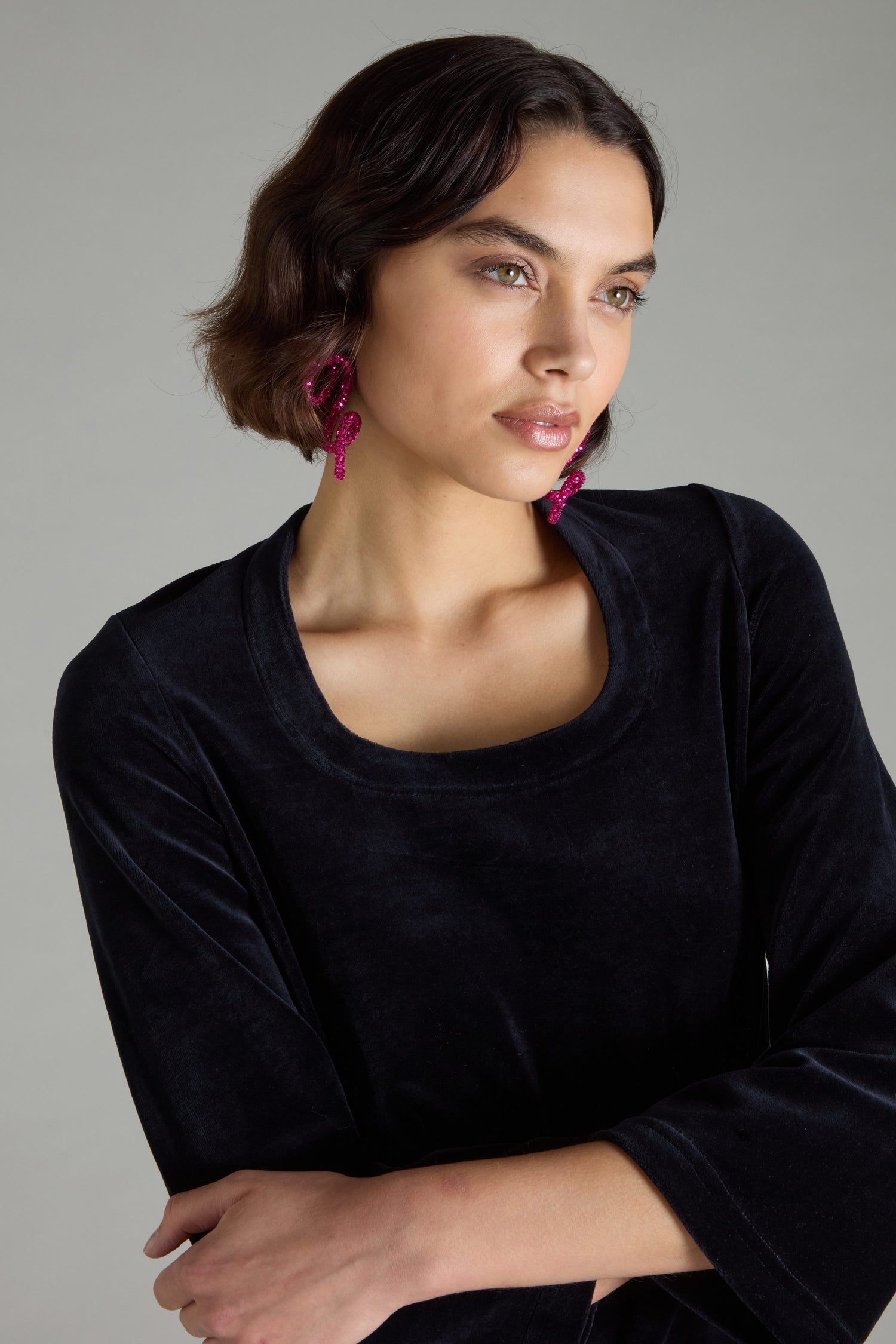 A person with short brown hair wearing a black top and Pink Disco Sketch Earrings by Samuel Coraux gazes to the side, exuding an air of avant-garde glamour.