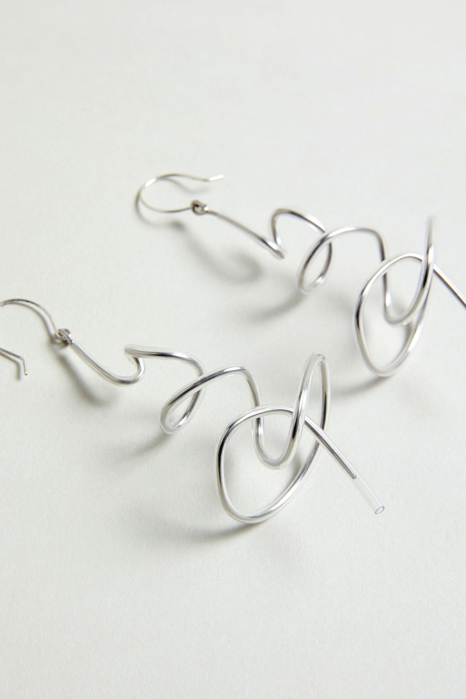 The Squiggle Earrings are silver, abstract-shaped statement drops displayed on a light neutral background—perfect for contemporary style.