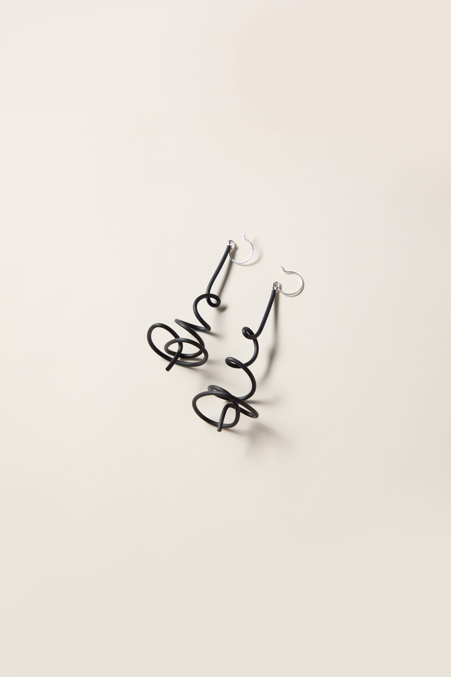 A pair of Squiggle Earrings, featuring black, curly wire designs with silver hooks on a light background, perfectly embodying the playful essence of Samuel Coraux's abstract jewellery.